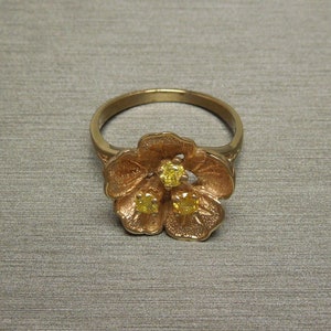 May include: A gold ring with a flower design featuring three yellow gemstones.