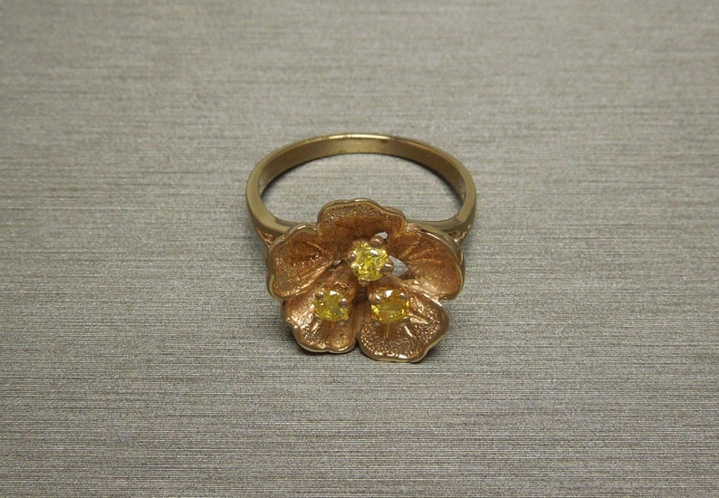May include: A gold ring with a flower design featuring three yellow gemstones.