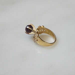 May include: A gold ring with a dark purple gemstone set in a delicate, ornate design.