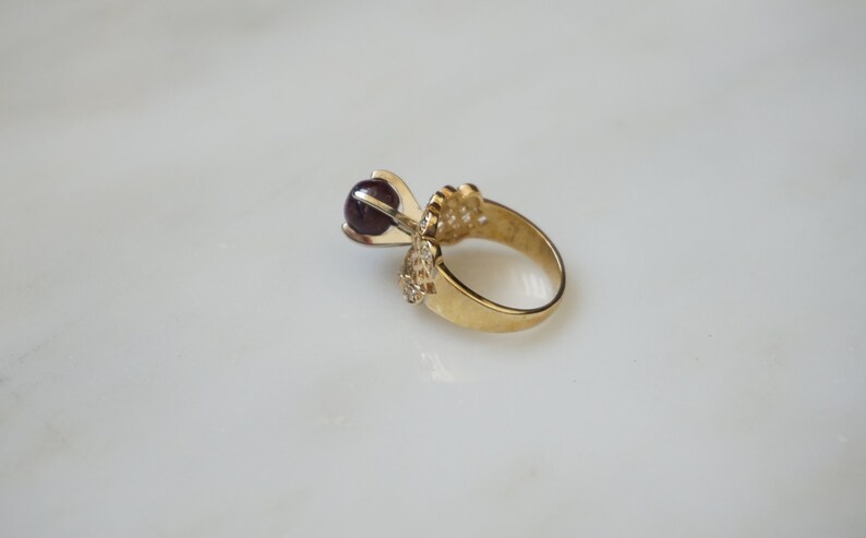 May include: A gold ring with a dark purple gemstone set in a delicate, ornate design.