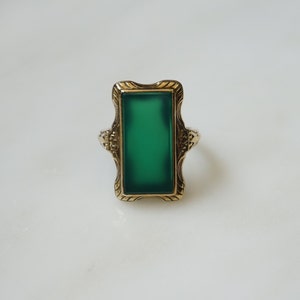 May include: A gold ring with a green rectangular stone set in a decorative frame.