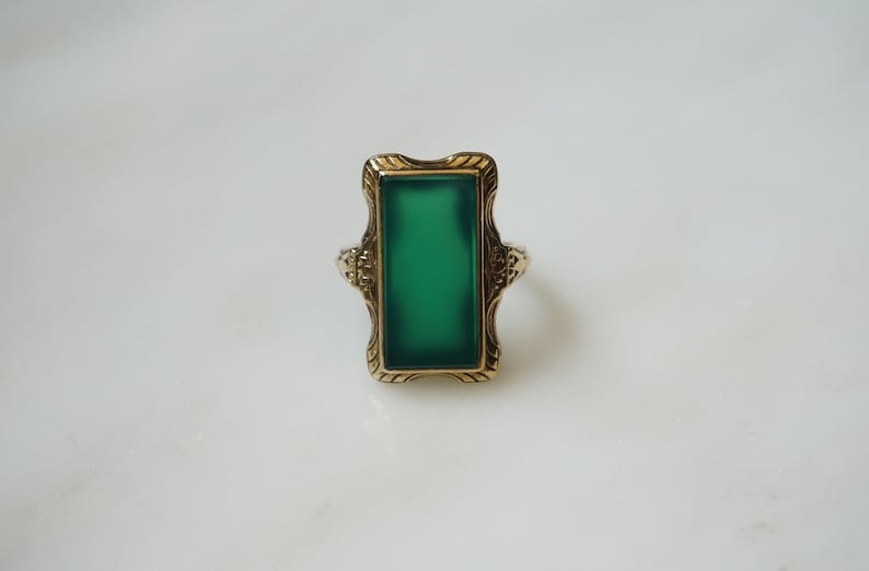 May include: A gold ring with a green rectangular stone set in a decorative frame.