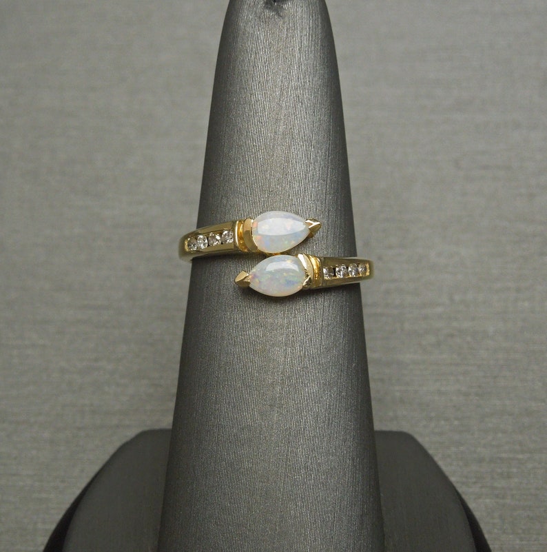 K&ouml;nnte beinhalten: Ein goldener Ring mit zwei birnenf&ouml;rmigen Opalen und einer Reihe kleiner Diamanten auf jeder Seite.