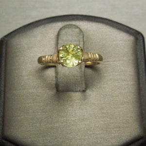 May include: A gold ring with a round, light green gemstone set in the center. The band is textured with small, raised dots.