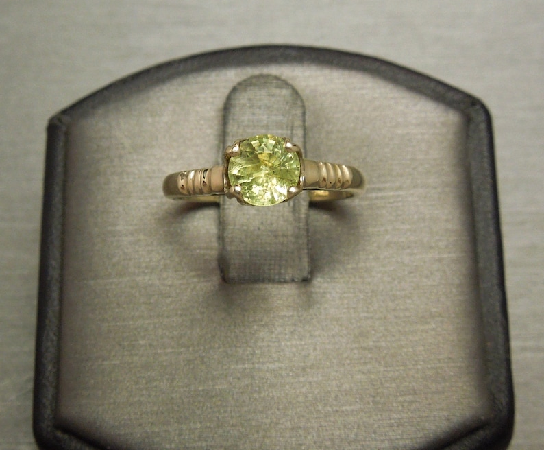 May include: A gold ring with a round, light green gemstone set in the center. The band is textured with small, raised dots.