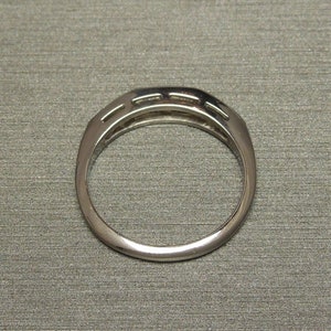 May include: A silver band ring with a row of small diamonds set in a channel setting.