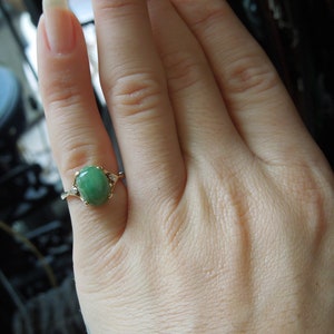 K&ouml;nnte beinhalten: Ein goldener Ring mit einem gr&uuml;nen ovalen Edelstein und kleineren Diamanten auf der Ringschiene.