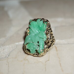 May include: A green jade ring with a floral design set in a gold filigree setting.