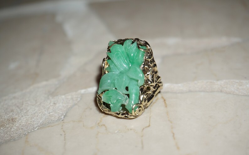 May include: A green jade ring with a floral design set in a gold filigree setting.