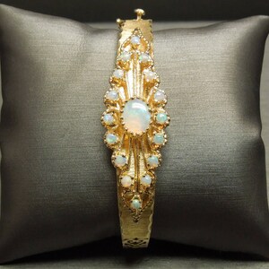 May include: A gold bracelet with a large opal gemstone surrounded by smaller opals. The bracelet has a delicate, ornate design.