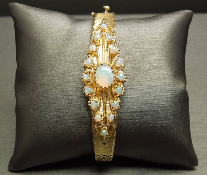 May include: A gold bracelet with a large opal gemstone surrounded by smaller opals. The bracelet has a delicate, ornate design.