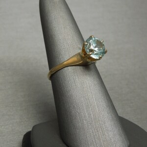 May include: A gold ring with a light blue gemstone set in a prong setting.