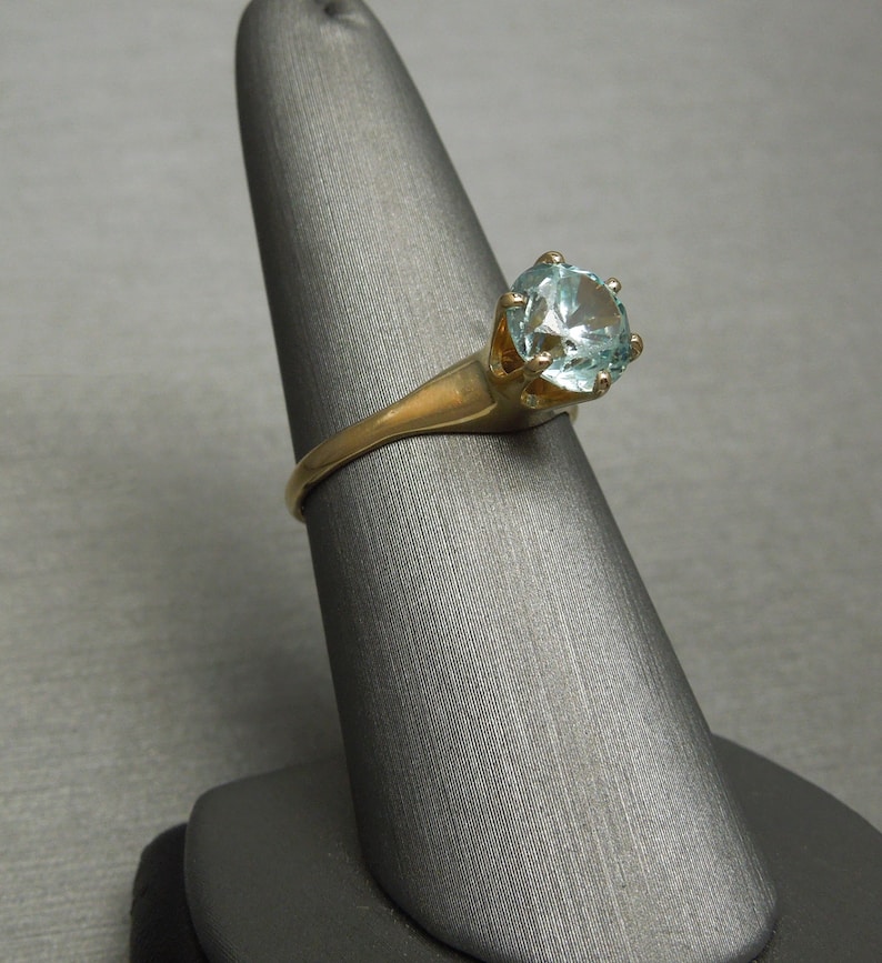 May include: A gold ring with a light blue gemstone set in a prong setting.