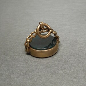 May include: A gold-toned seal with a dark green stone and a chain attached to the top.