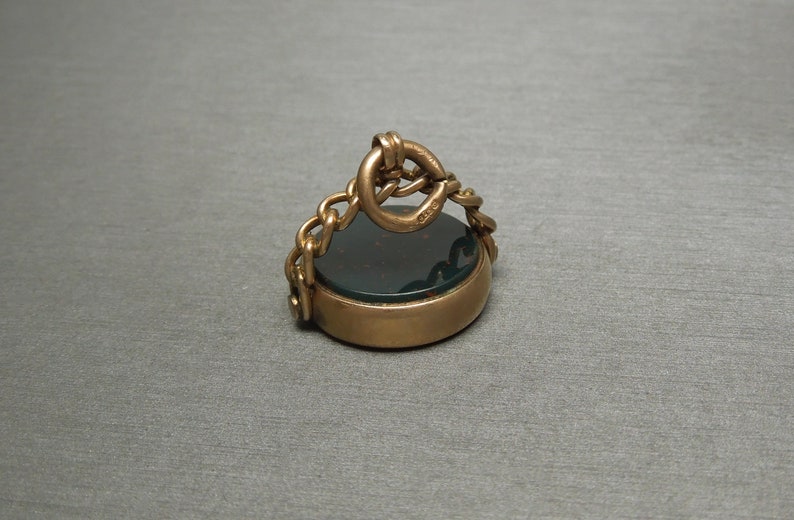 May include: A gold-toned seal with a dark green stone and a chain attached to the top.