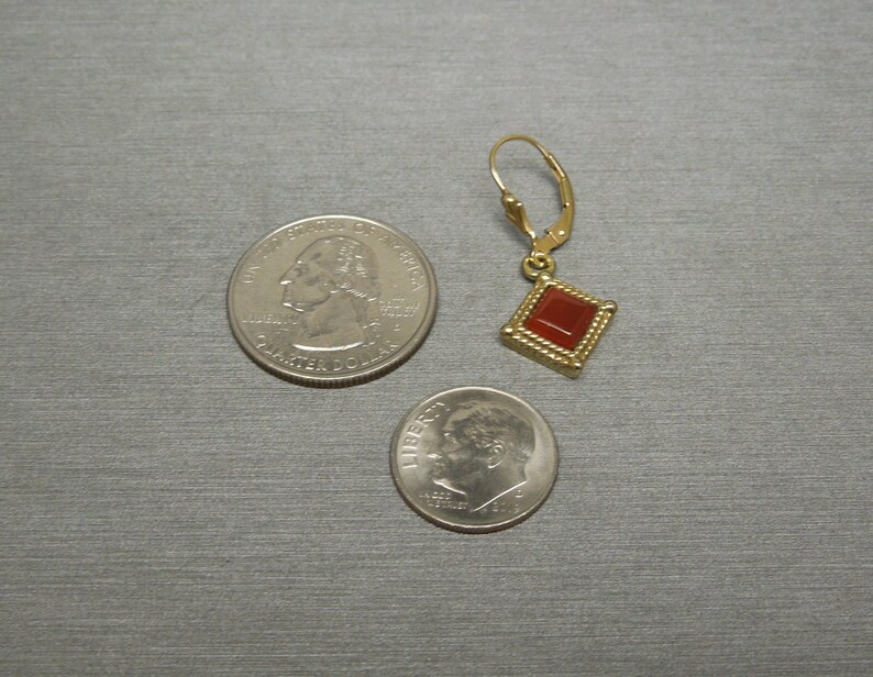 May include: Gold dangle earring with a red square gemstone. The earring is shown next to a US quarter and a US dime for size reference.