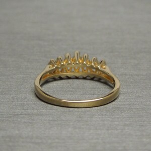 May include: A gold ring with a row of small, pointed elements along the top. The ring has a smooth, polished band and a detailed design on the top. The ring is set against a gray background.