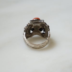 May include: Silver ring with an intricate design and a red gemstone.