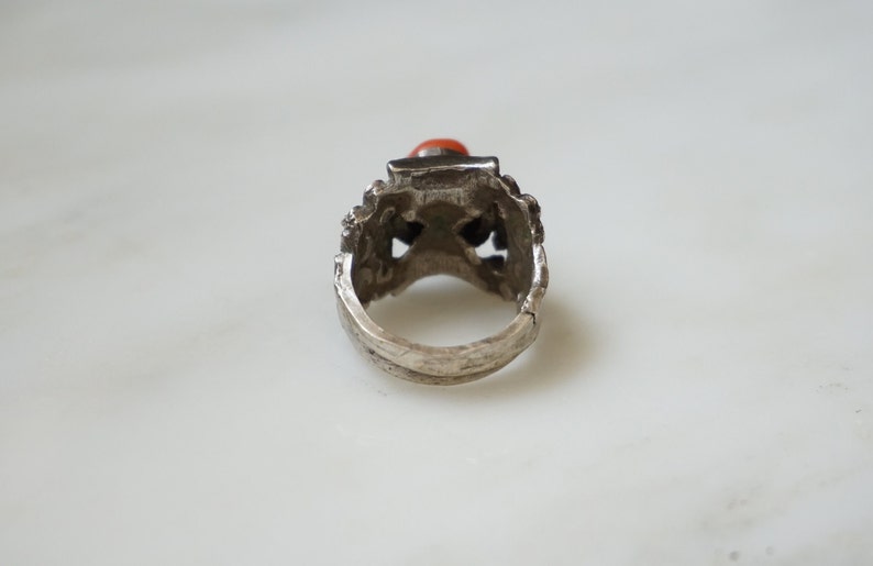 May include: Silver ring with an intricate design and a red gemstone.
