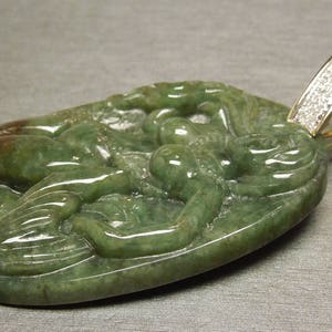 May include: A green jade pendant carved with a detailed design of a dragon, set in a gold pendant with a diamond-encrusted bail.