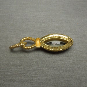 May include: A gold-tone pendant featuring a clear faceted gemstone set in a rope-like frame.