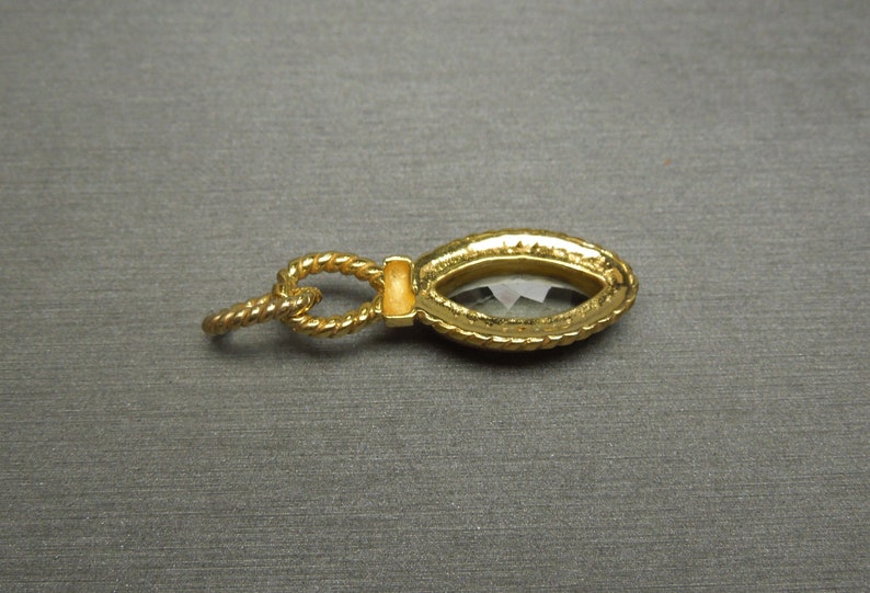 May include: A gold-tone pendant featuring a clear faceted gemstone set in a rope-like frame.