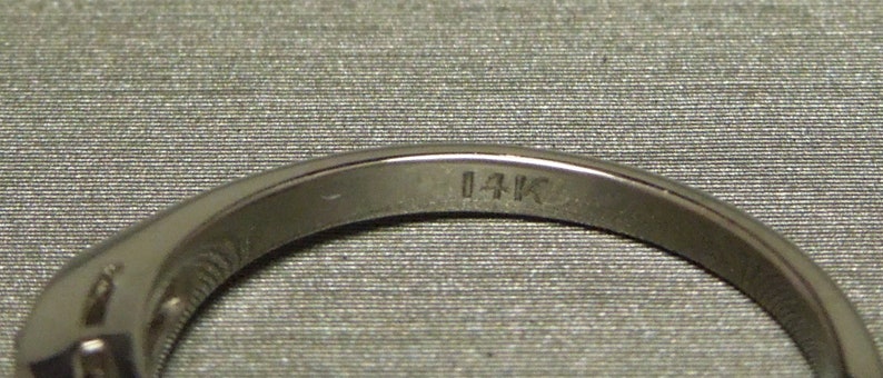 May include: Close-up of the inside of a silver ring with the inscription "14K" on the band.