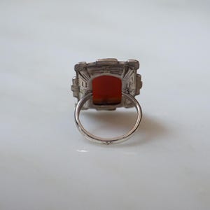 May include: A silver ring with a square-shaped red gemstone set in a geometric design.