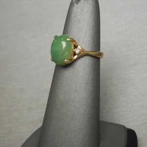K&ouml;nnte beinhalten: Ein goldener Ring mit einem gr&uuml;nen ovalen Jade-Stein und einem kleinen Diamanten-Akzent.