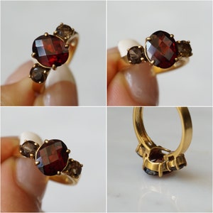 May include: A gold ring with a large oval-shaped garnet gemstone and two smaller brown gemstones. The ring is set in a simple band.