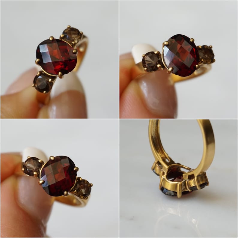 May include: A gold ring with a large oval-shaped garnet gemstone and two smaller brown gemstones. The ring is set in a simple band.