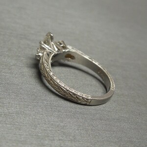 Pode incluir: Um anel de noivado de prata com uma pedra central de diamante e diamantes menores na banda. A banda &eacute; decorada com um design floral intrincado.