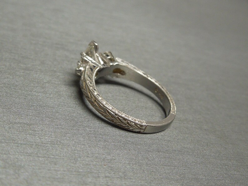 Pode incluir: Um anel de noivado de prata com uma pedra central de diamante e diamantes menores na banda. A banda &eacute; decorada com um design floral intrincado.