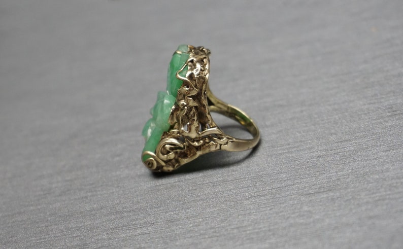 May include: A gold ring with a green jade stone set in a floral design.