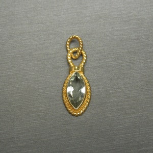May include: A gold pendant featuring a green gemstone in a marquise shape. The pendant has a rope-like design around the gemstone and a loop at the top for attaching a chain.