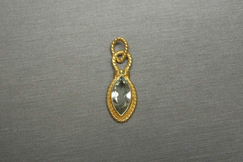 May include: A gold pendant featuring a green gemstone in a marquise shape. The pendant has a rope-like design around the gemstone and a loop at the top for attaching a chain.