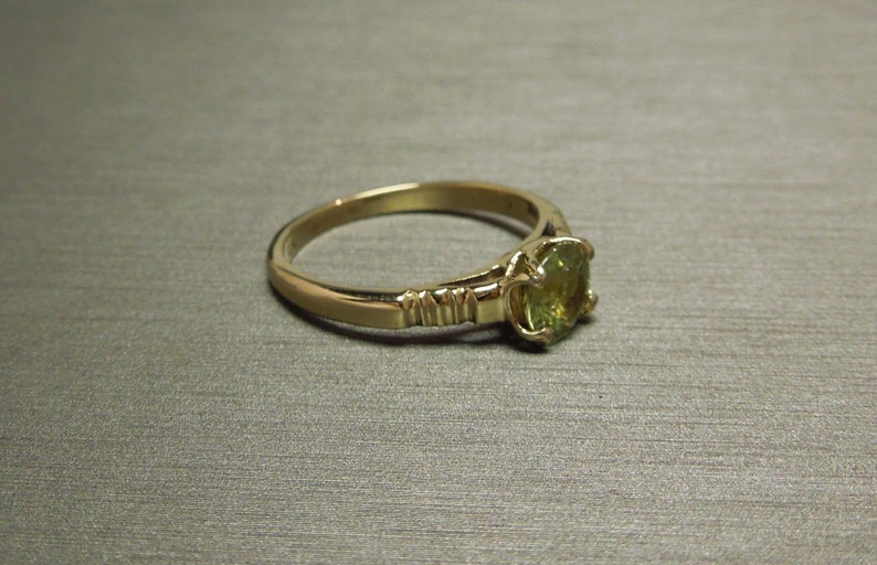 May include: A gold ring with a green gemstone set in a prong setting. The band is textured with a series of small ridges.