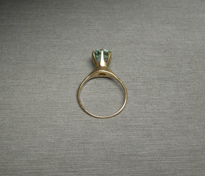 May include: A gold ring with a light blue gemstone set in a prong setting.