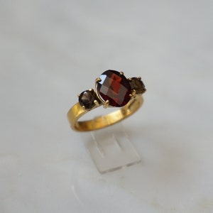 May include: A gold ring with a large red gemstone and two smaller brown gemstones.