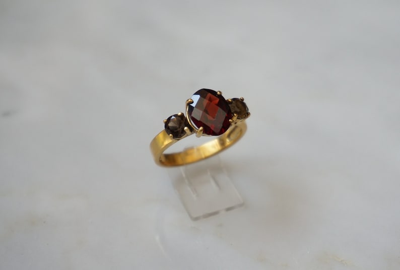 May include: A gold ring with a large red gemstone and two smaller brown gemstones.
