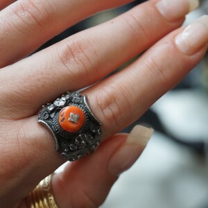 May include: A silver ring with an intricate design and a bright orange stone in the center.