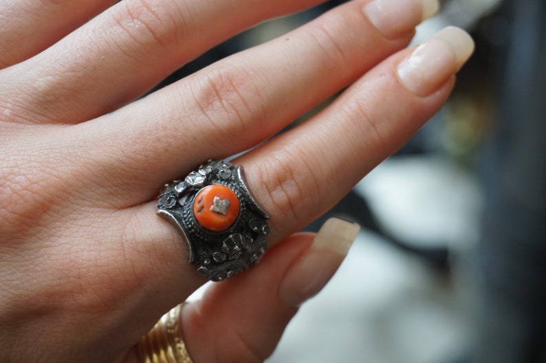 May include: A silver ring with an intricate design and a bright orange stone in the center.