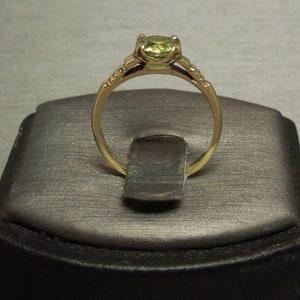 May include: A gold ring with a green gemstone set in a prong setting. The ring has a delicate band with a milgrain edge.