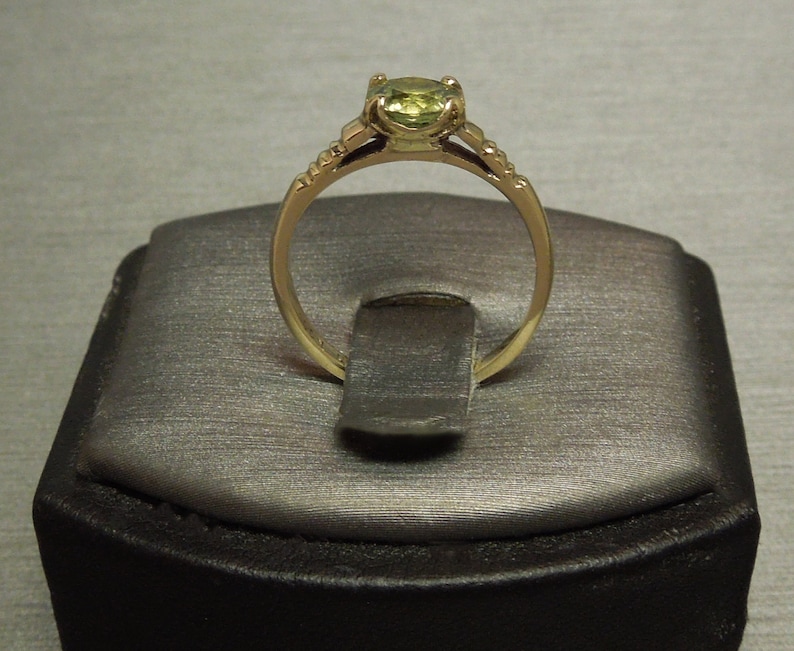 May include: A gold ring with a green gemstone set in a prong setting. The ring has a delicate band with a milgrain edge.