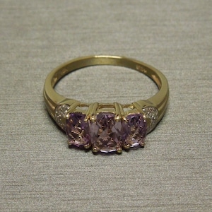 May include: A gold ring with three rectangular purple gemstones and small diamonds on the band.