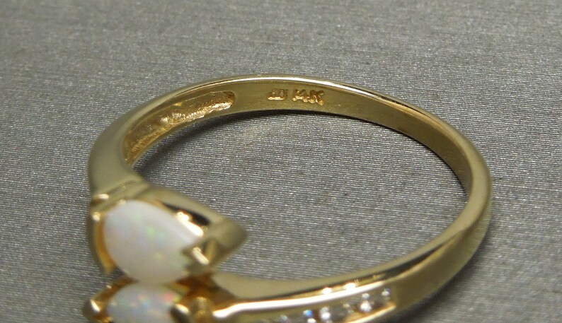 K&ouml;nnte beinhalten: Ein goldener Ring mit zwei birnenf&ouml;rmigen Opalen und einer Reihe kleiner Diamanten. Der Ring ist innen mit "14K" gekennzeichnet.