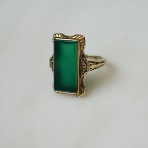 May include: A gold ring with a green rectangular stone set in a decorative filigree design.
