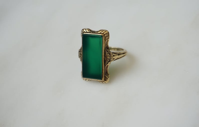 May include: A gold ring with a green rectangular stone set in a decorative filigree design.