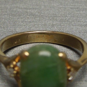 K&ouml;nnte beinhalten: Ein goldener Ring mit einem gr&uuml;nen Edelstein und kleinen Diamanten an den Seiten. Der Ring ist innen mit "14K" gekennzeichnet.