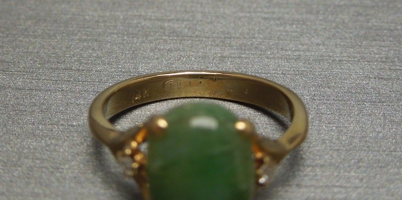 K&ouml;nnte beinhalten: Ein goldener Ring mit einem gr&uuml;nen Edelstein und kleinen Diamanten an den Seiten. Der Ring ist innen mit "14K" gekennzeichnet.